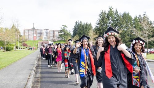 Graduates process in a line towards the ceremony, with Old Main in the background