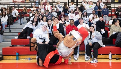 Marty the Mascot poses with a group of students in bleachers at Pack the Pavilion