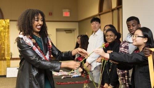 An Act Six Scholar receives garlands and a rose from a line of her peers