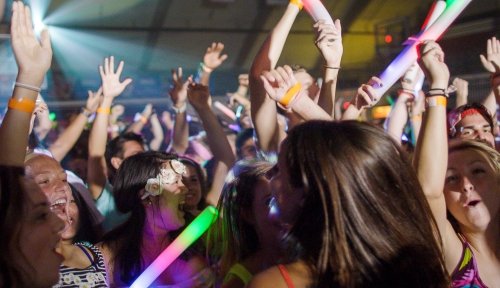 A large group of students dance with glowsticks, their hands in the air