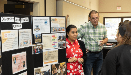 Crystal Cardona and John Hopkins answer a student's question in front of a resource board for the Diversity and Equity Center