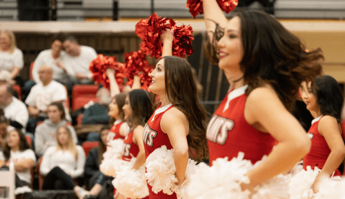 Saints cheerleaders in a line raise red pompoms in the air, white pompoms on their hips