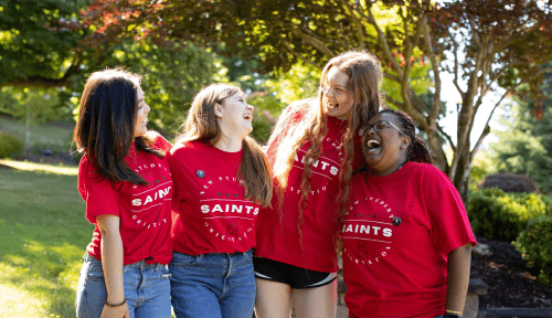 Four Saints in red shirts laugh outside with their arms around each other
