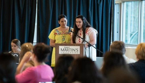 Two students speak at a lectern in front of a crowd
