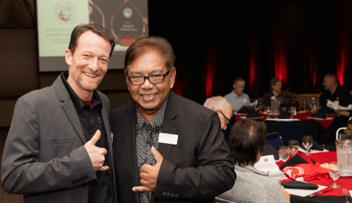 Two alums pose in front of a sea of tables at an awards dinner