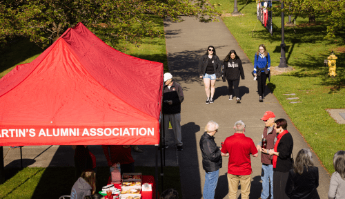 Students and alumni gather around a red tent that reads: Alumni Association