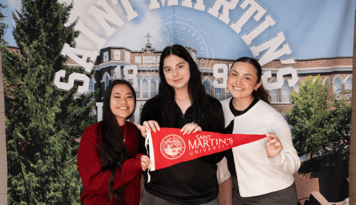 Three students hold an SMU pennant in front of a Saint Martin's University backdrop