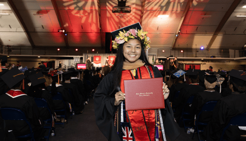 A graduate in regalia holding the diploma at graduation