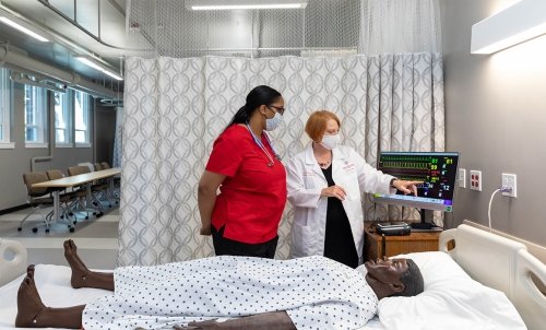 Dr. Teri Woo instructs a nursing student at the bedside of a mannikin in the nursing lab.