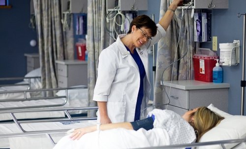 A nurse smiles as she takes care of a patient in a hospital setting.