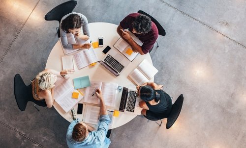 Overhead view of five students studying with books and laptops at a round table.