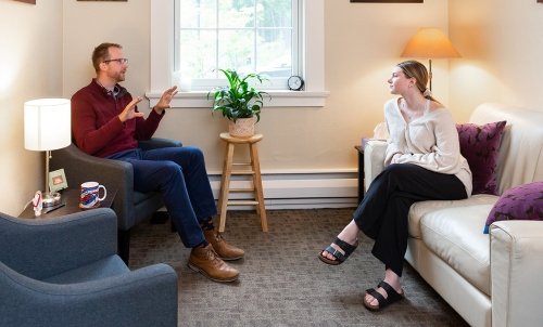 A counselor and client on a couch talk in a calm, well-lit room.