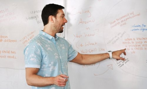 A professor teaches in front of a whiteboard with lots of text written on it.