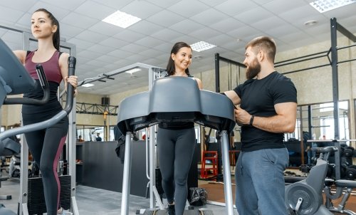 A physical trainer instructs a woman on a treadmill at the gym.