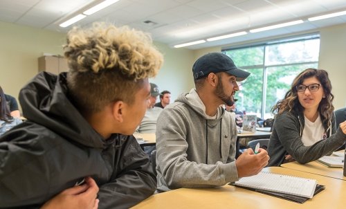 Three students discuss at desks during class.