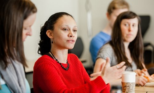 A student speaks in class while her peers seated beside her look on.