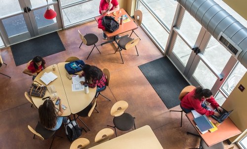 Top down view from second floor of Harned Hall, picturing three students working at a round table and individual students at smaller tables around them.