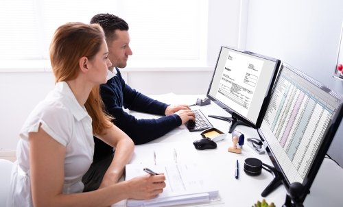 AcademicProgram_InternalAuditManagement_dreamstime_xl_181788113.jpg A teacher demonstrates something on a two-screened computer while a student takes notes.