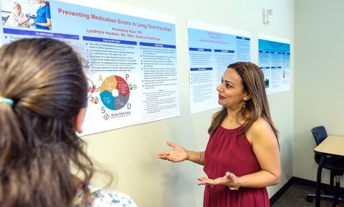 A person stands in front of several nursing academic posters, giving a presentation.