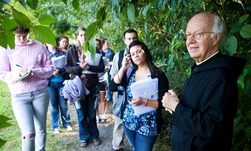 Fr. Kilian instructs a group of students outside, surrounded by leaves.