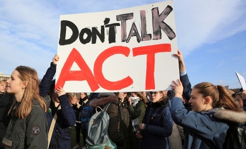 A group of students--primarily women--hold up a sign that says "Don't Talk - ACT"