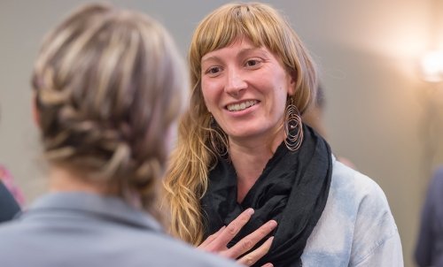 A female student puts her hand to her scarf as she speaks to a person who has their back to the camera.