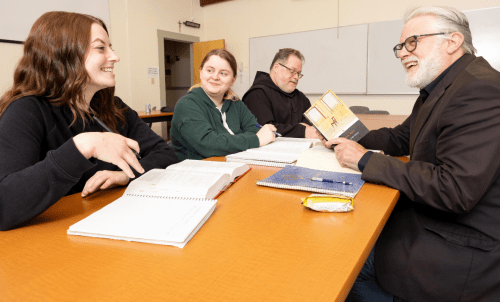 Literary Studies hero 3 1160x702.png Students and professor discuss literature at a table with books and notebooks