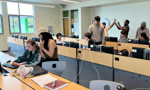 Students work in a computer classroom, cables crossing desks to create a network