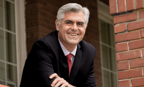 President Brownsberger leans on railing with brick building behind him
