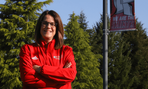 Theresa Hanson stands in Saints apparel in front of trees and a &quot;We are the Saints&quot; banner