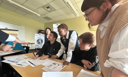 Students work on document around a table, with one holding up climate posters