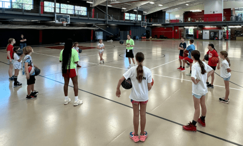 Young campers stand in circle around coach on basketball court