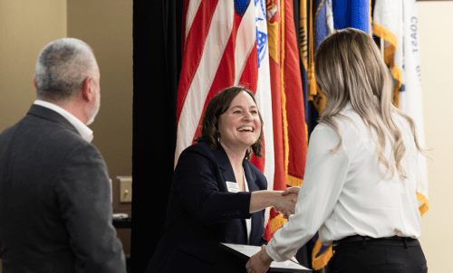Staff shake hands with a student in front of a row of flags
