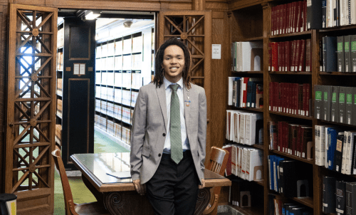 Student in a suit standing in wood-paneled library