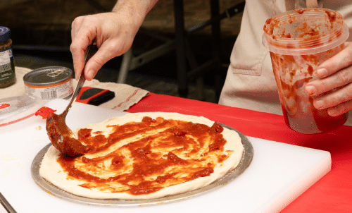 Red sauce being spread on pizza dough