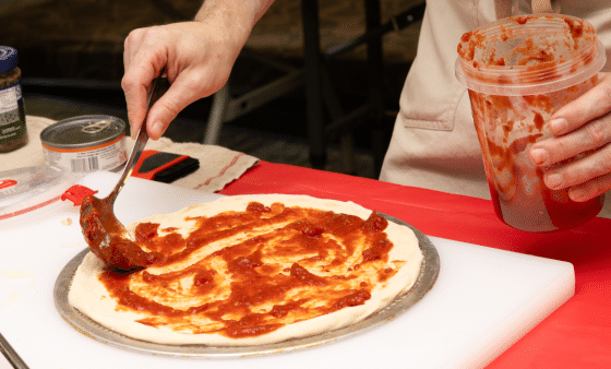 Red sauce being spread on pizza dough