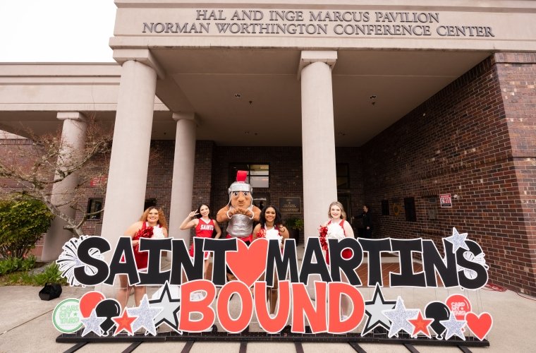Cheerleaders and Marty stand behind a giant Saint Martin's Bound sign, bubblies floating in the air