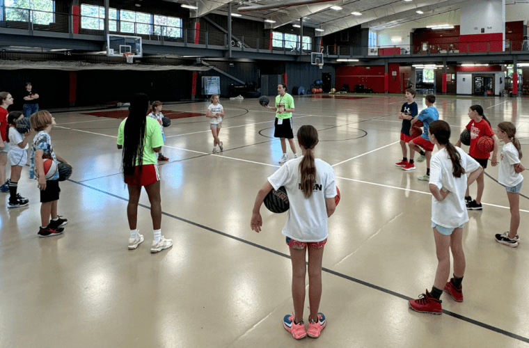 Young campers stand in circle around coach on basketball court