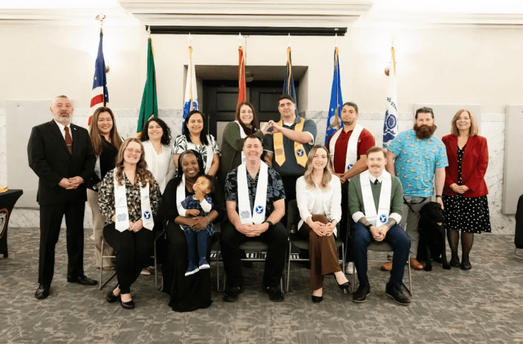 A group of students and staff stand in front of flags