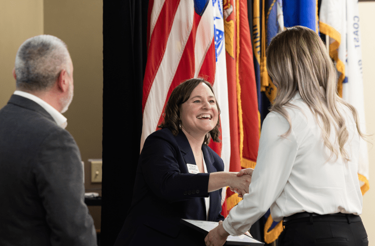 Staff shake hands with a student in front of a row of flags
