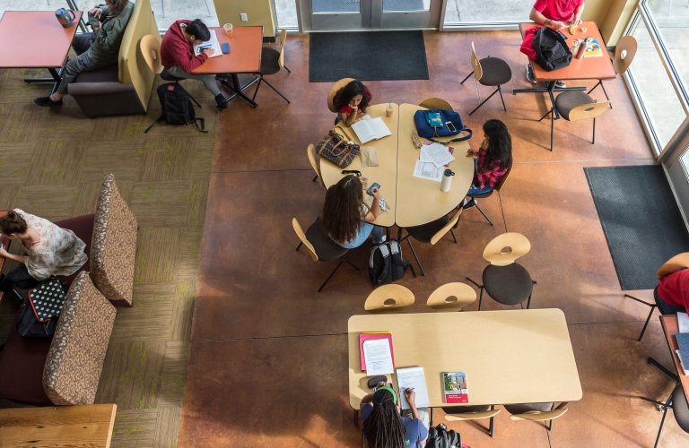 Overhead view of sitting area in Harned hall with lots of students grouped at various tables working alone or in company.
