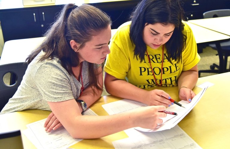Two students seated at a desk work on a paper.