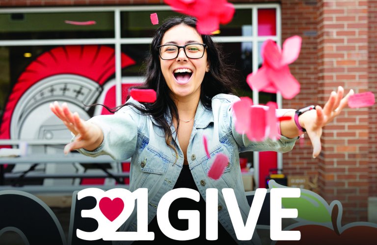 A student scatters red tickets in the air above the 3.21GIVE logo