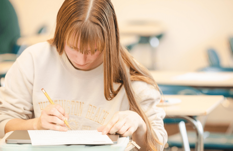 A student works with a pencil and notebook at a classroom desk