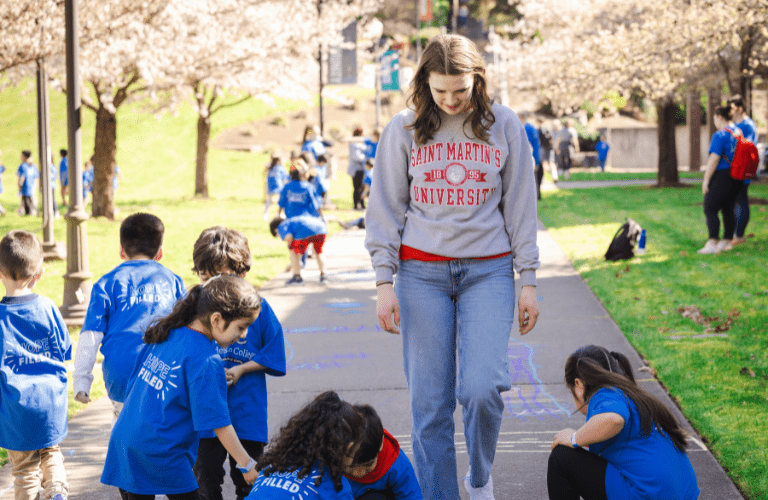 A student supervises a group of children in blue shirts outside on a sunny day