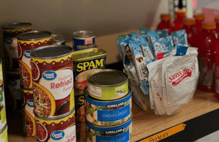 A shelf showing canned beans, spam, hot chocolate, and more