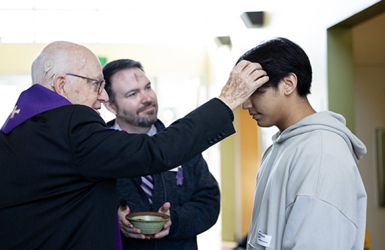 A priest puts ashes on students forehead for Ash Wednesday