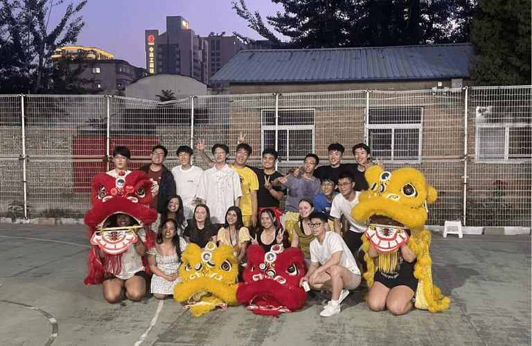 A group of students with people in yellow and red dragon costumes outside at twilight