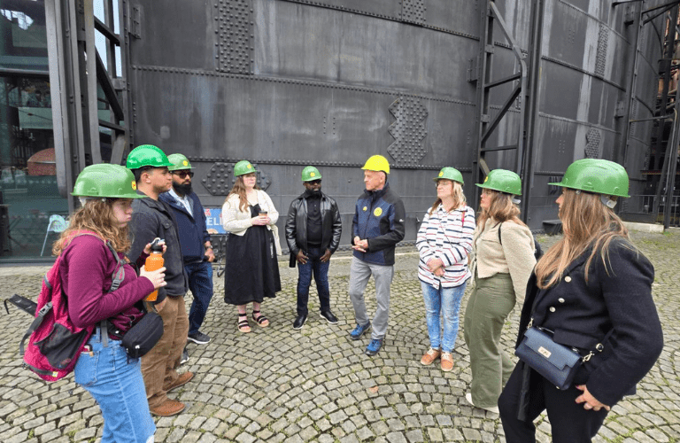 A group of students in hard hats stand in front of industrial building