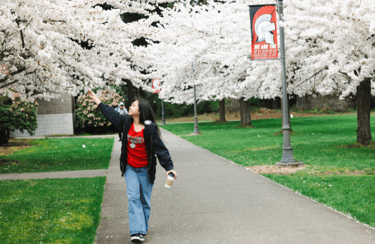 A student walks along a path lined by blossoming trees